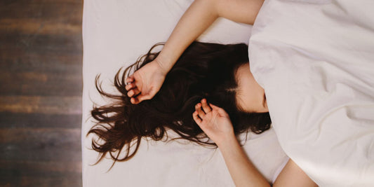 Mujer conectando con su cuerpo en un momento íntimo de placer y autodescubrimiento, recostada con expresión de calma y gozo