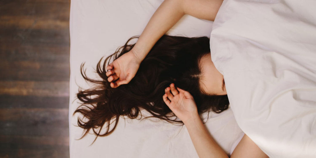 Mujer conectando con su cuerpo en un momento íntimo de placer y autodescubrimiento, recostada con expresión de calma y gozo